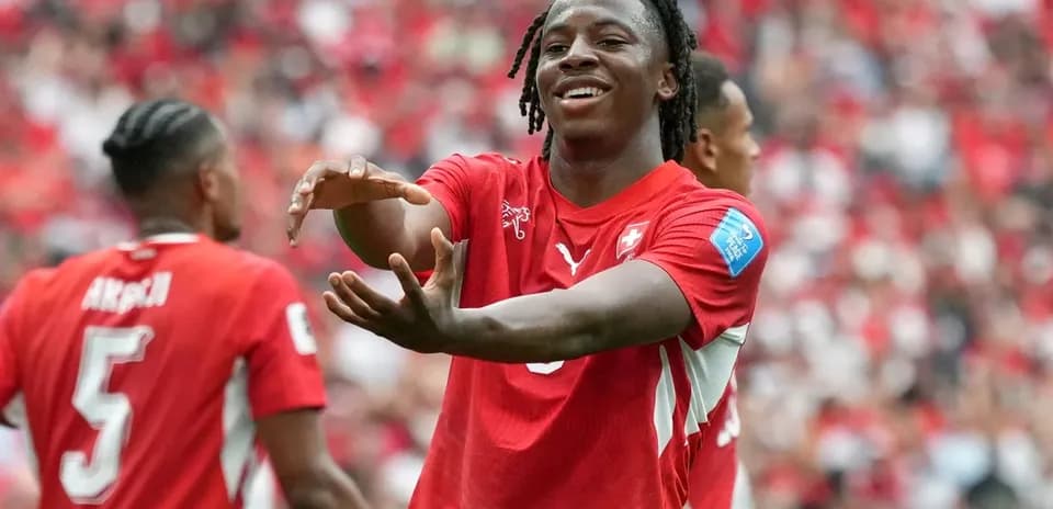 Futbolçu qol sevincini paylaşır, arxa planda komanda yoldaşları