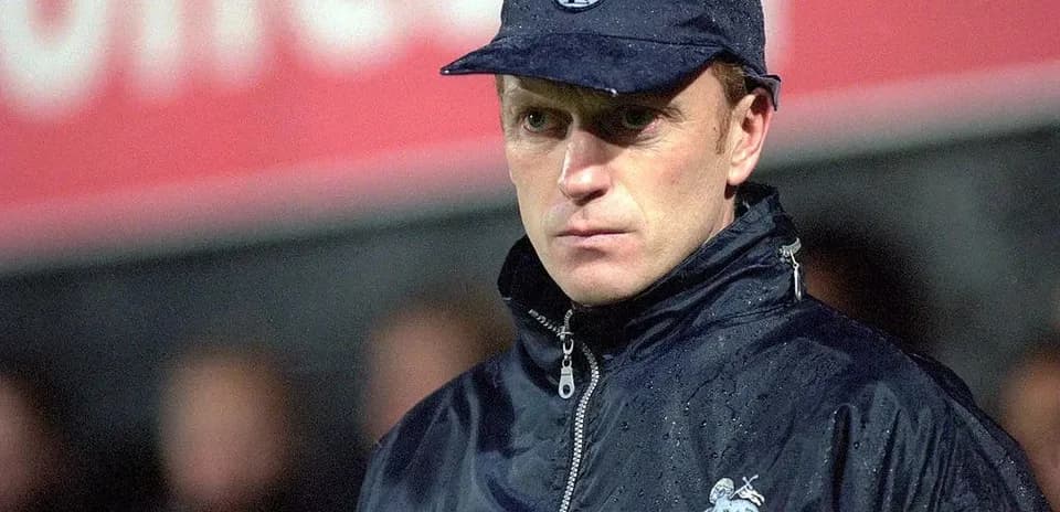 Football manager in rain jacket and cap during match