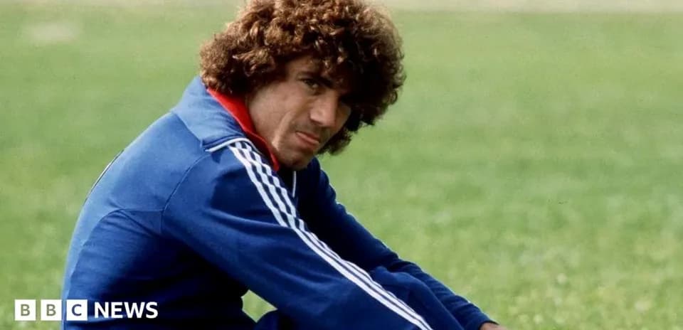 Football player sitting on grass, wearing blue tracksuit