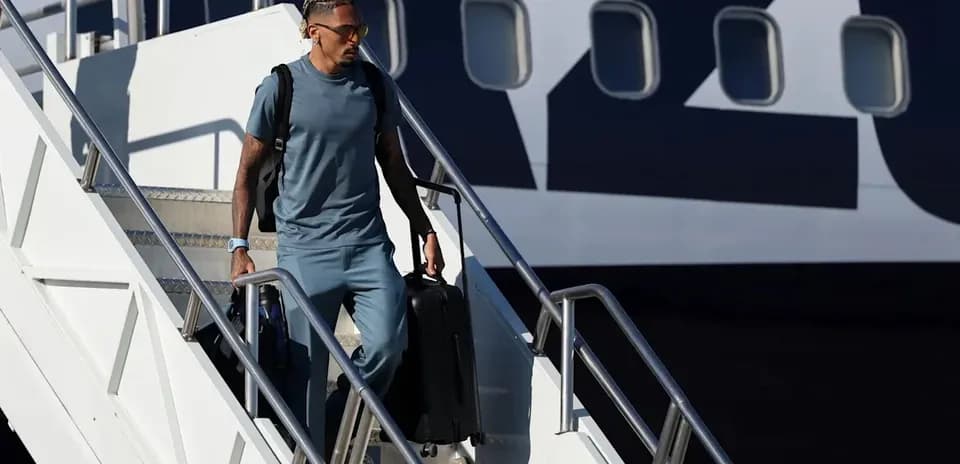 Player disembarking from airplane with suitcase