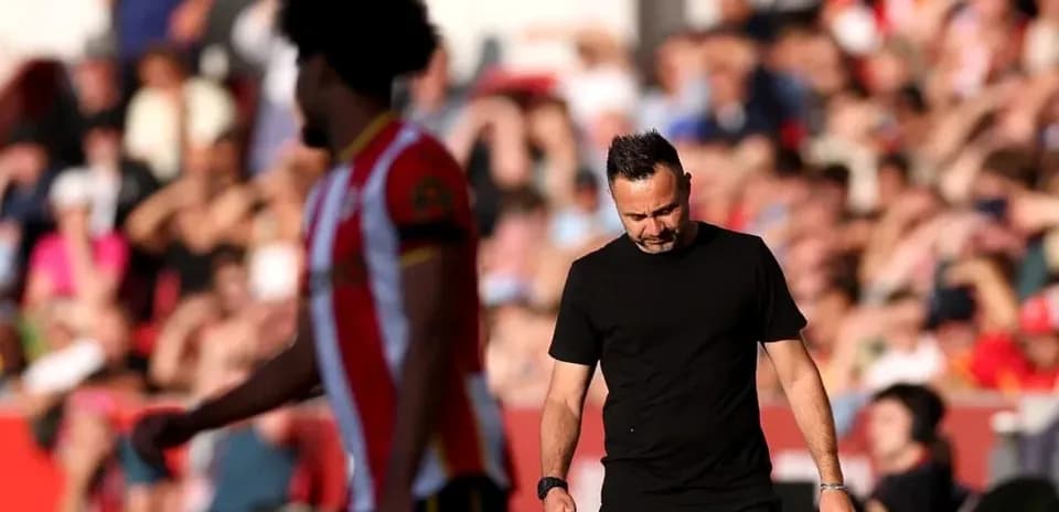 Coach walking past player during match with fans