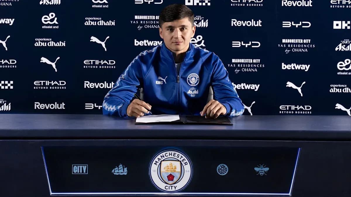 Futbolçu imza atarkən mətbuat konfransında oturur