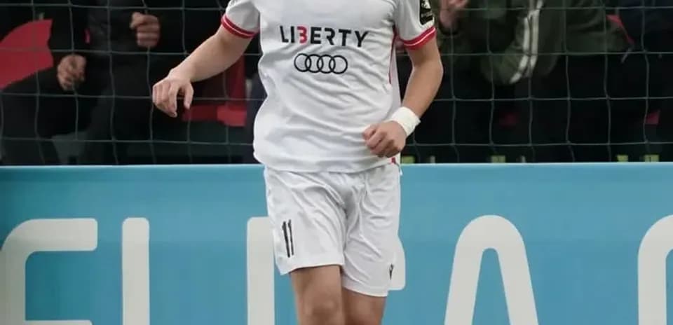 Futbolçu topu idarə edir, arxa planda azarkeşlər var
