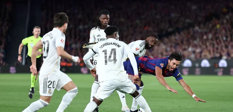 Barcelona player falling as Real Madrid defenders approach