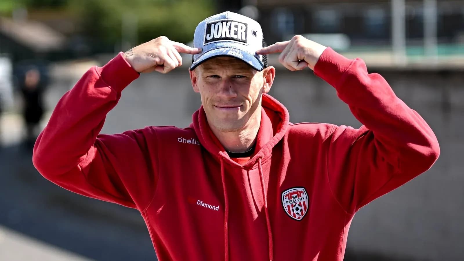 Person wearing 'JOKER' cap and red hoodie
