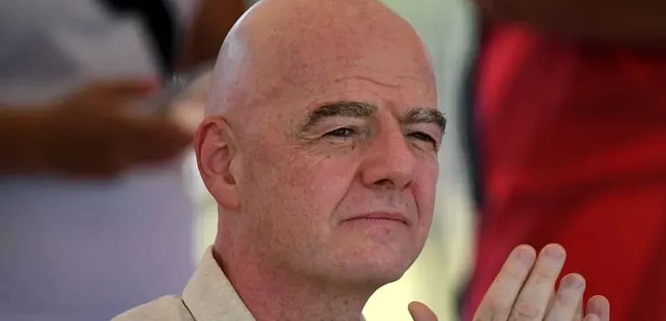 Bald man with hands clasped, seated outdoors