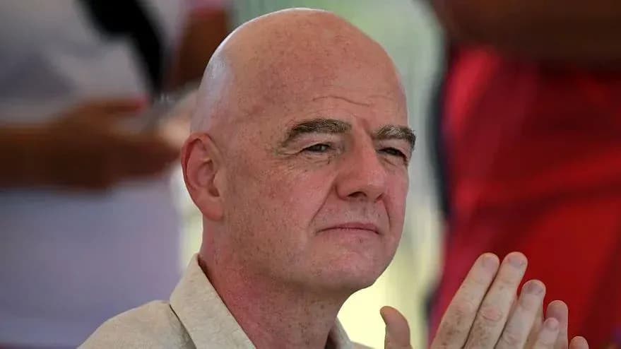 Bald man with hands clasped, seated outdoors