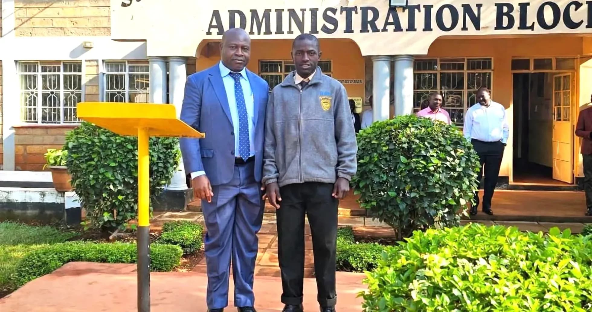Two men posing in front of school administration block