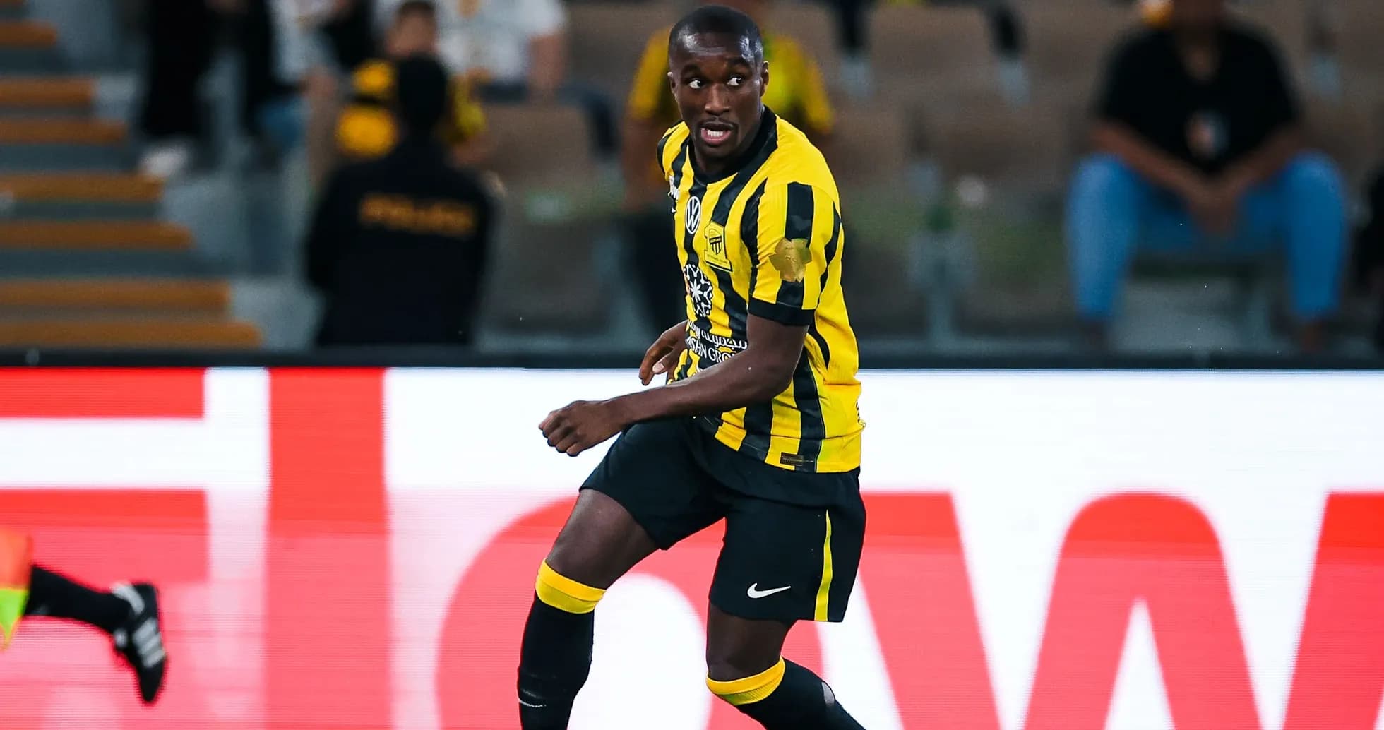 Futbolçu topa yönəlir, qara və sarı forma geyinib