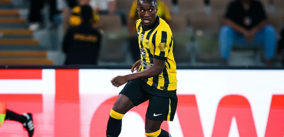 Futbolçu topa yönəlir, qara və sarı forma geyinib