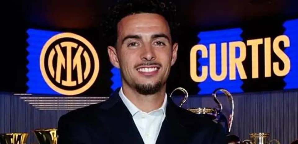 Curtis smiling in front of trophies and logo