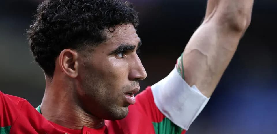 Futbolçu qırmızı forma ilə meydanda əllərini qaldırır
