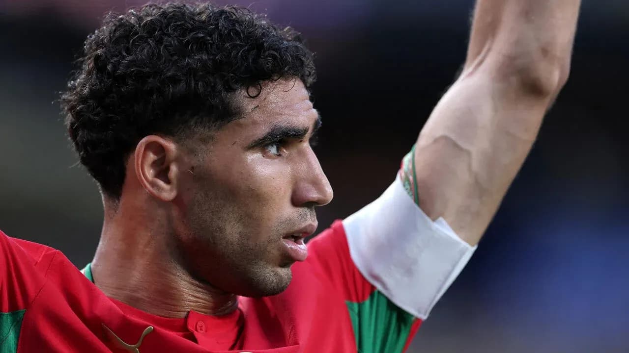 Futbolçu qırmızı forma ilə meydanda əllərini qaldırır