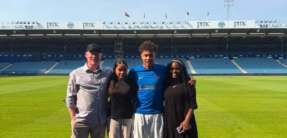 Four people posing on football pitch at stadium