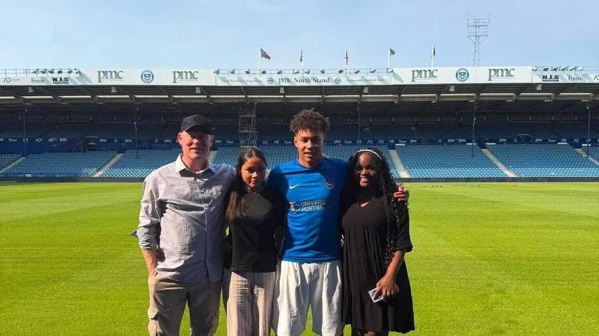 Four people posing on football pitch at stadium