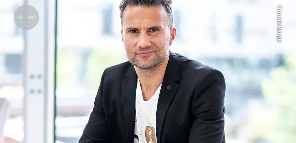 Man in blazer seated indoors, looking at camera