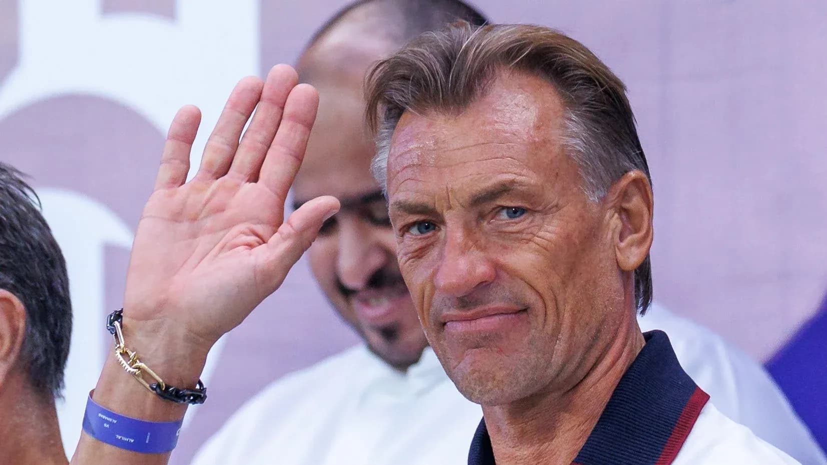 Coach waving during event with team members behind