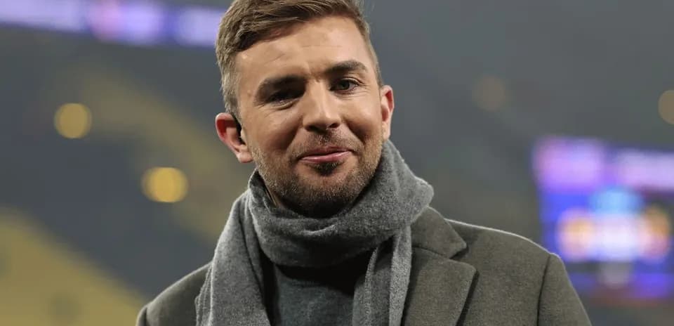 Man in a coat and scarf smiling at event Man in a coat and scarf smiling at event