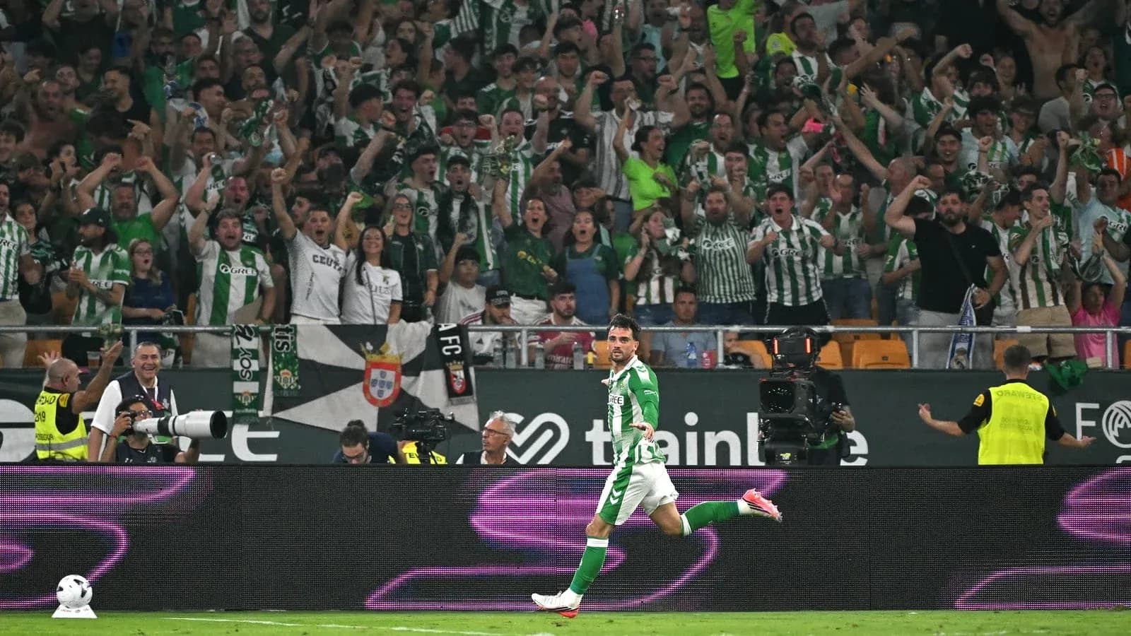 Futbolçu qolu qeyd edir, arxa planda azarkeşlər Futbolçu qolu qeyd edir, arxa planda azarkeşlər