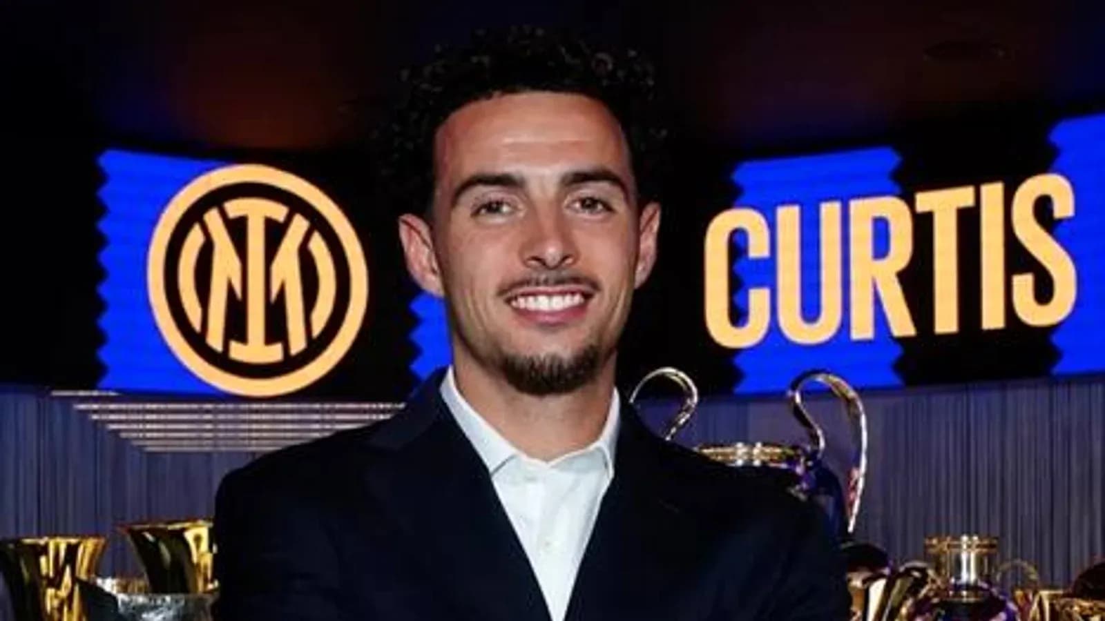 Curtis smiling in front of trophies and logo Curtis smiling in front of trophies and logo