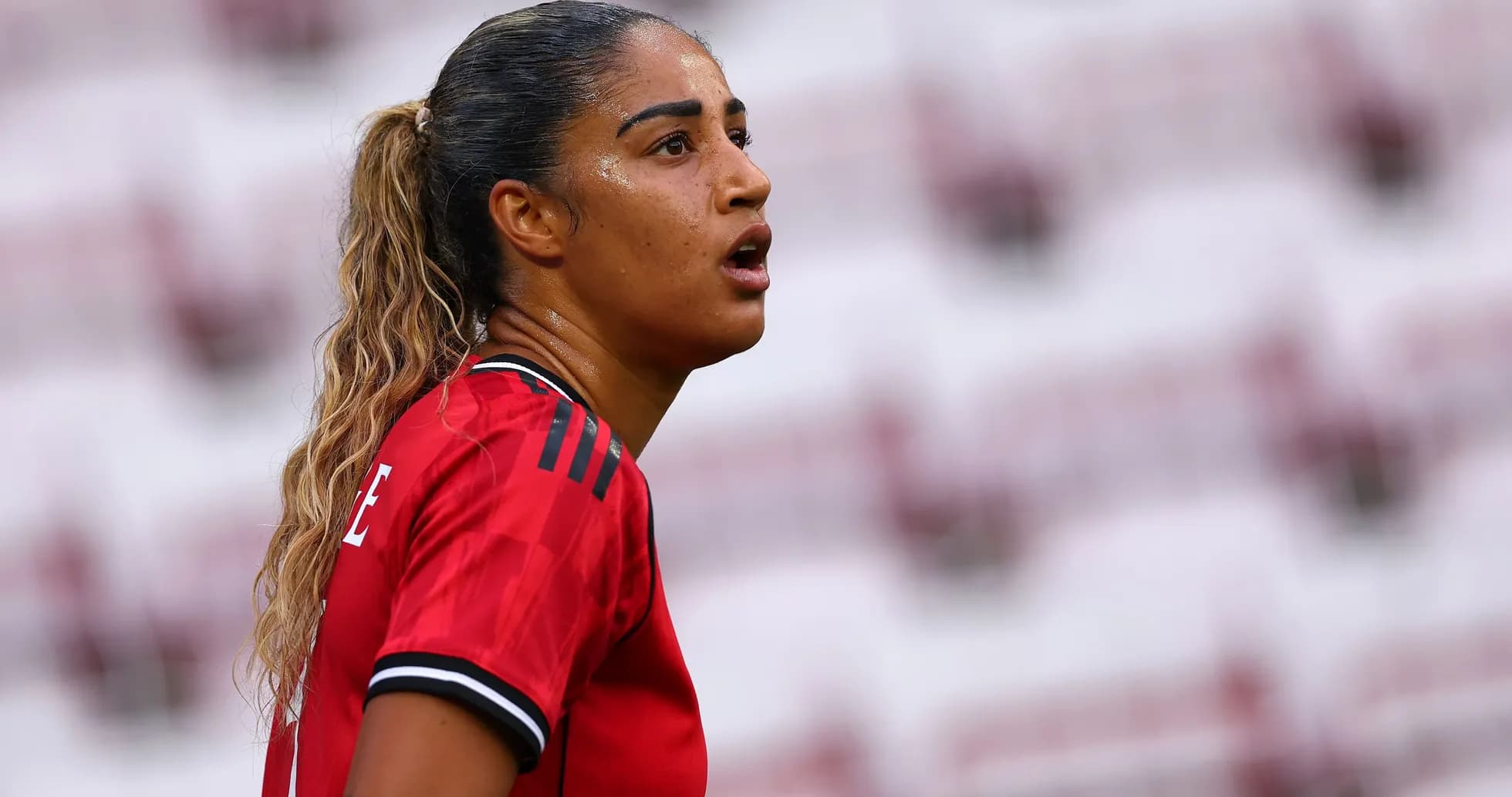 Futbolçu oyunda diqqətlə baxır, qırmızı forma geyinib Futbolçu oyunda diqqətlə baxır, qırmızı forma geyinib