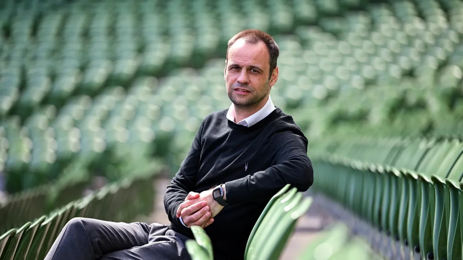 Man sitting on stadium seats, wearing black sweater Man sitting on stadium seats, wearing black sweater